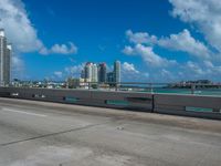 an empty freeway with two lane street alongside the large city skyline in the distance while blue sky and clouds above