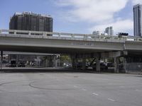 an empty parking lot with buildings in the background and a road running under it next to a bridge