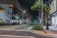 a city street lined with palm trees and a man walking in the crosswalk at night