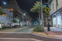 a city street lined with palm trees and a man walking in the crosswalk at night