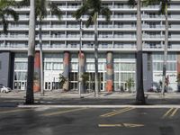 palm trees line the sidewalk outside a tall building with a bright orange and white banner