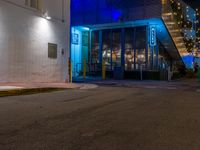 a city street with an illuminated sidewalk and a building in the background at night time