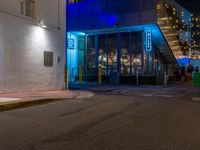 a city street with an illuminated sidewalk and a building in the background at night time