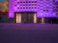 the purple lights are shining on an empty parking lot near a building with a garage