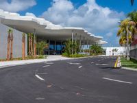 a road going into the building on which there are palm trees, and one of which is made from concrete