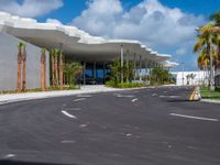 a road going into the building on which there are palm trees, and one of which is made from concrete