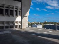 empty parking lot near large concrete building on sunny day with blue sky and clouds above