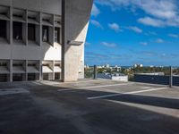 empty parking lot near large concrete building on sunny day with blue sky and clouds above