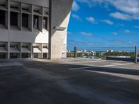 empty parking lot near large concrete building on sunny day with blue sky and clouds above