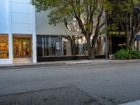 an empty street with a bench, building, and tree in the front yard in the distance