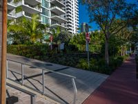 the entrance to an apartment with palms trees and bushes in the foreground, next to a concrete driveway