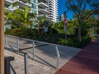 the entrance to an apartment with palms trees and bushes in the foreground, next to a concrete driveway