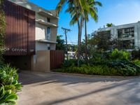 the entrance to an apartment with palms trees and bushes in the foreground, next to a concrete driveway