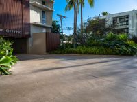 the entrance to an apartment with palms trees and bushes in the foreground, next to a concrete driveway