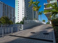 the entrance to an apartment with palms trees and bushes in the foreground, next to a concrete driveway