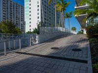 the entrance to an apartment with palms trees and bushes in the foreground, next to a concrete driveway