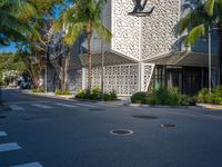 a street view of an architectural building with palm trees in the front and a yellow van parked in front