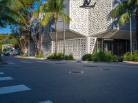 a street view of an architectural building with palm trees in the front and a yellow van parked in front