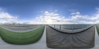 a large skateboard park with two ramps for a skate boarder and a blue sky with fluffy cloud - filled clouds