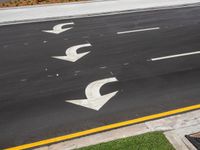 an image of a long street with arrows painted in white paint on the pavement near a brick structure