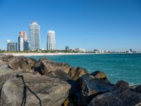 a person sitting on rocks by the water near the city skyline and buildings in miami, florida