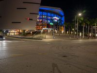 the view of an outside mall with cars coming in and out of it at night