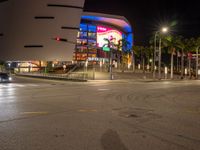 the view of an outside mall with cars coming in and out of it at night