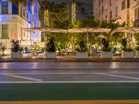 a bench with umbrellas sitting at night in the middle of town street next to trees