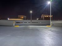 an empty parking lot with lights above it at night time on the other side of a city street