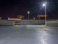 an empty parking lot with lights above it at night time on the other side of a city street