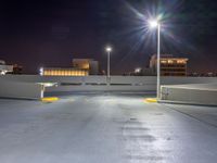 an empty parking lot with lights above it at night time on the other side of a city street