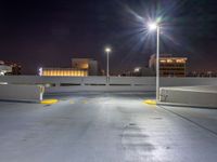 an empty parking lot with lights above it at night time on the other side of a city street