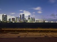 this is the view of a city across the bay from a bench at dusk in a city park