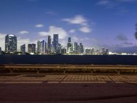 this is the view of a city across the bay from a bench at dusk in a city park