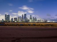 this is the view of a city across the bay from a bench at dusk in a city park