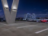 some cars parked on the asphalt at night with buildings in the background near a bridge