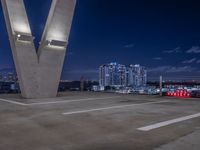 some cars parked on the asphalt at night with buildings in the background near a bridge