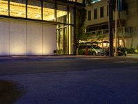 there is a car parked at the curb by the building lit up at night with the windows open