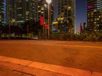 city skyline with various tall buildings with lights at night from the curb of a street