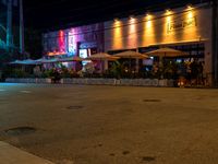 people are standing in front of a restaurant at night in a city street next to the sidewalk