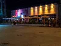 people are standing in front of a restaurant at night in a city street next to the sidewalk