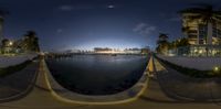 the night sky over a river with palm trees and apartment buildings in the background and clouds overhead