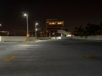 a empty parking lot with a street light and tall buildings at night in the background