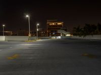 a empty parking lot with a street light and tall buildings at night in the background