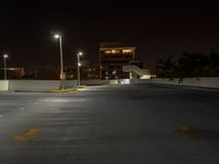 a empty parking lot with a street light and tall buildings at night in the background