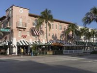 some palm trees outside the front of a very pretty restaurant with awnings on it