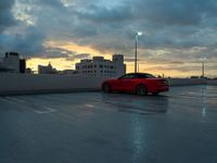 a red car parked in an empty parking lot near a cityscape at dusk