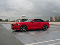 a red mustang convertible car in front of an airport in a cloudy day of the same time