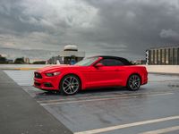 a red mustang convertible car in front of an airport in a cloudy day of the same time