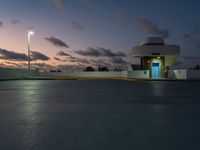 a large building at dusk in an empty parking lot near a street light and parking lot